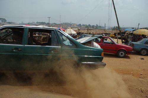 Départ en trombe, Route de l’aéroport, Lagos Une voiture démarre devant nous, le coffre chargé des provisions du marché